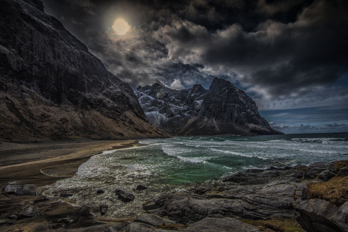 brown rocky mountain beside body of water under cloudy sky during daytime
