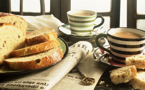 Image white and black ceramic mug beside bread on white ceramic plate