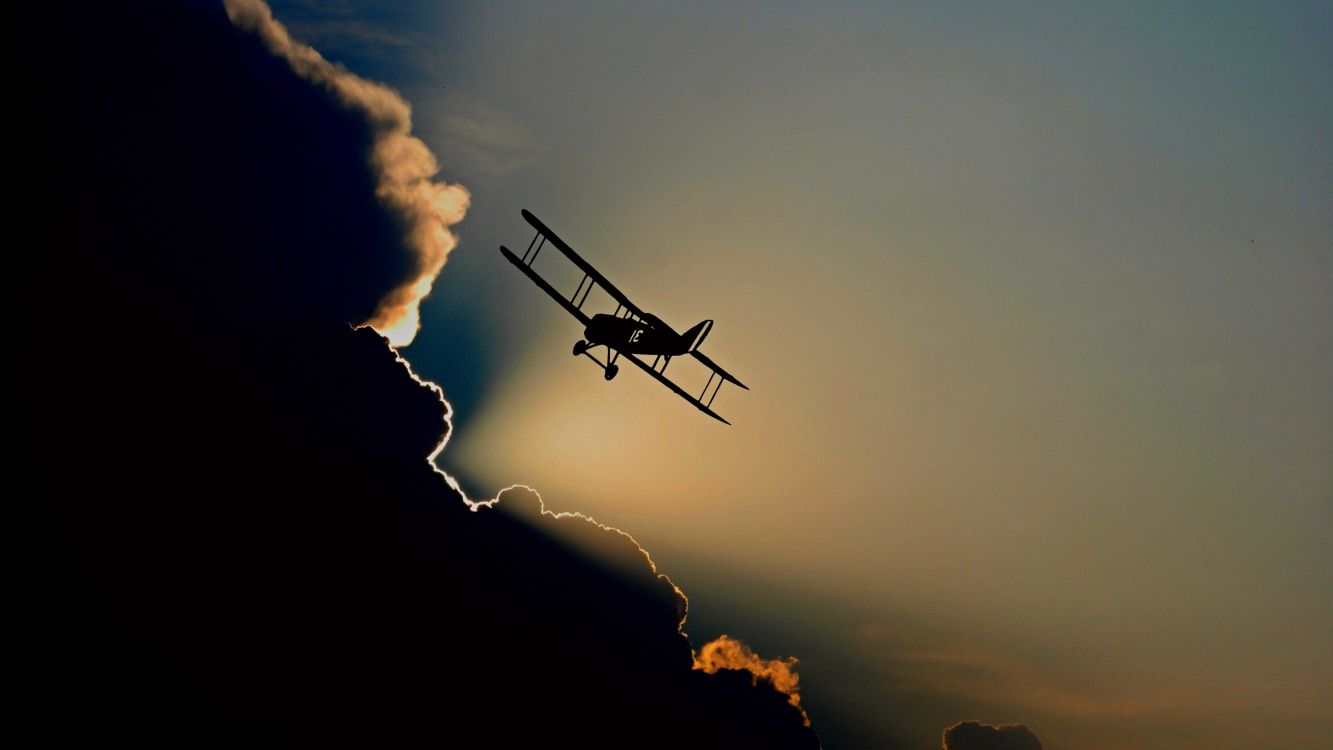 silhouette of airplane flying over the clouds during sunset