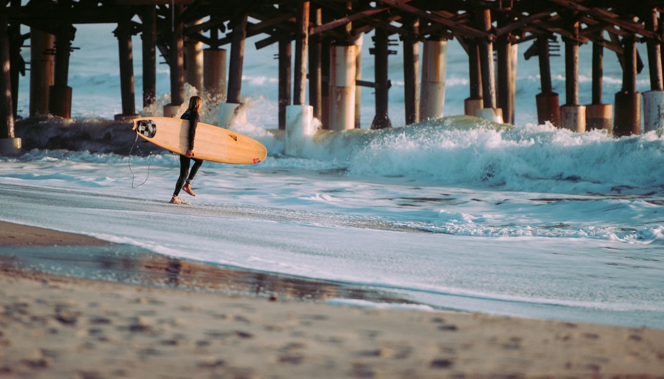 Personne Tenant Une Planche de Surf Blanche Marchant Sur la Plage Pendant la Journée. Wallpaper in 3977x2270 Resolution
