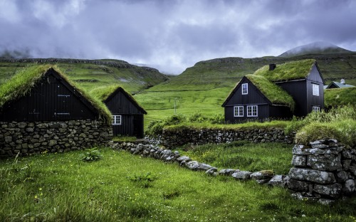 Image brown wooden house on green grass field near mountain under white clouds during daytime