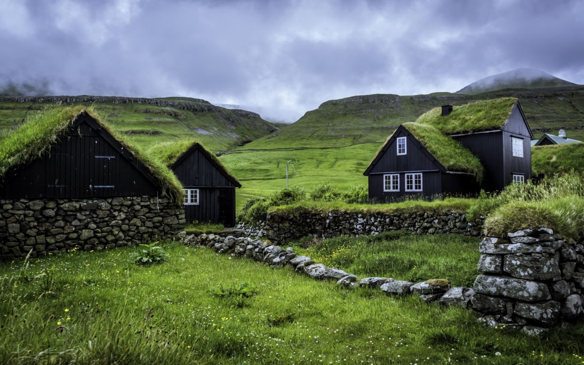 brown wooden house on green grass field near mountain under white clouds during daytime