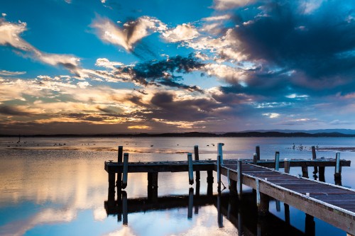 Image brown wooden dock on calm water under blue and white cloudy sky during daytime