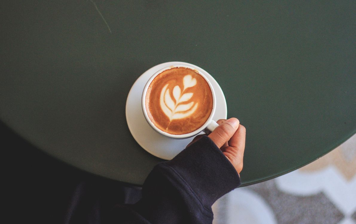 person holding white ceramic mug with brown liquid