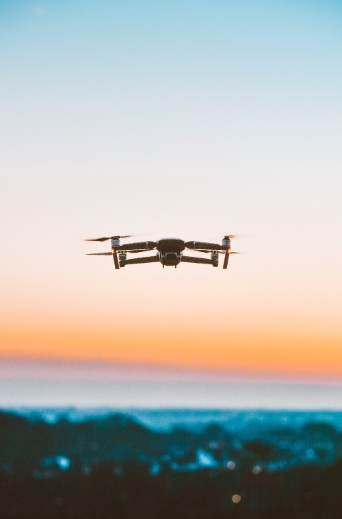 Image black drone flying over the sea during sunset