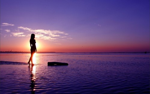 Image woman in black bikini standing on body of water during sunset