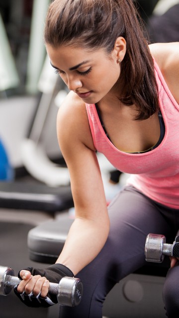 Image woman in pink tank top holding dumbbell