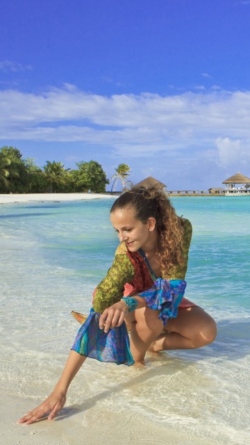 Image girl in blue and white polka dot dress sitting on beach shore during daytime