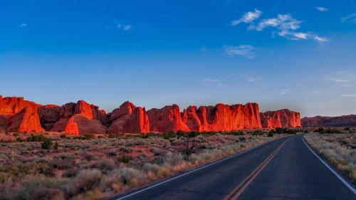 Image gray asphalt road between brown rock formation under blue sky during daytime