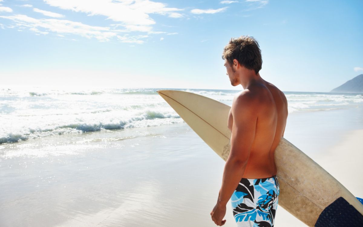 Mann in Blau-weißen Boardshorts Mit Weißem Surfbrett am Strand Tagsüberboard. Wallpaper in 2560x1600 Resolution