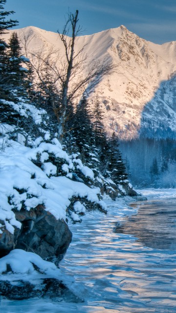 Image snow covered mountain near body of water during daytime