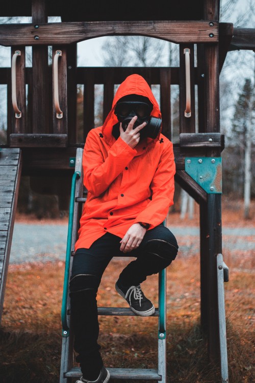 Image woman in orange hoodie and black pants sitting on brown wooden fence