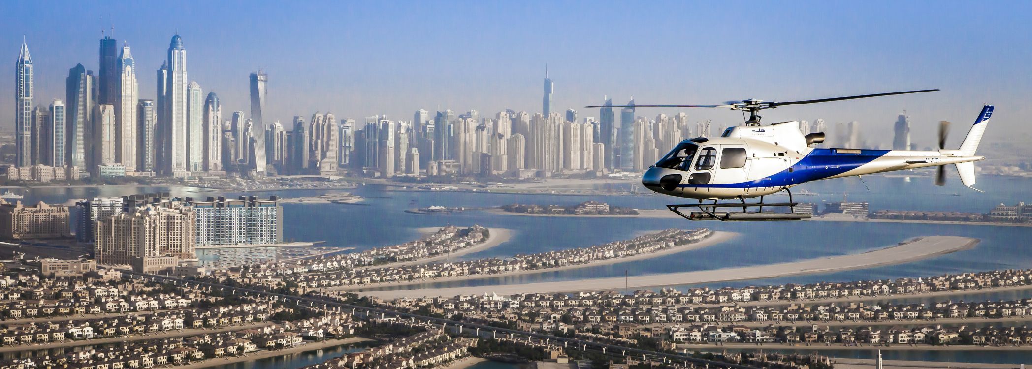 Helicóptero Blanco y Azul Sobrevolando Los Edificios de la Ciudad Durante el Día. Wallpaper in 5060x1810 Resolution