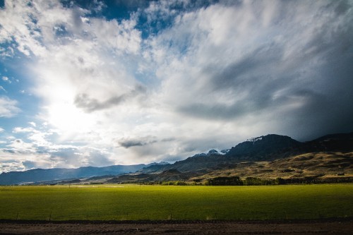 Image green grass field near brown mountain under white clouds and blue sky during daytime