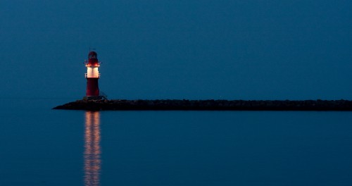 Image white and red lighthouse near body of water during night time