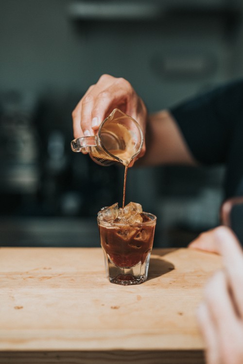 Image person pouring brown liquid on clear drinking glass