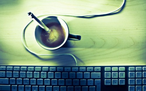 Image white ceramic mug on white ceramic saucer beside black computer keyboard