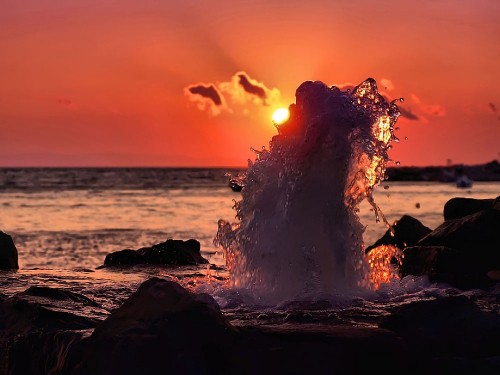 Image silhouette of person standing on rock near body of water during sunset